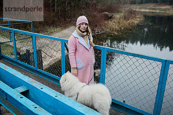 Junges Mädchen geht mit einem weißen  flauschigen Samojedenhund in der Natur spazieren