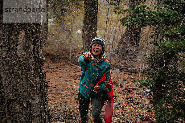 Lachendes Kind wirft Schneeball beim Wandern im Wald