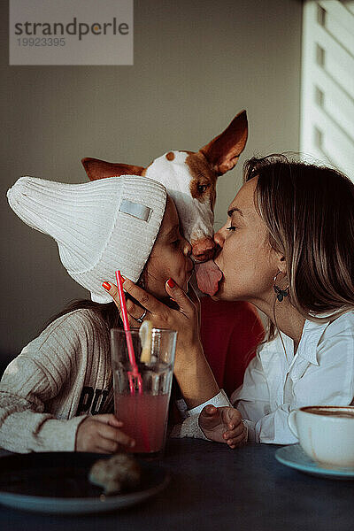 Mutter und Tochter im Café mit Hund. Mamas Kuss. Freundlich zu Tieren.