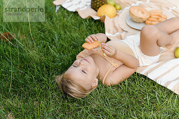 Zeit  Obst zu essen  süßes Mädchen isst Melone  während es im Gras liegt