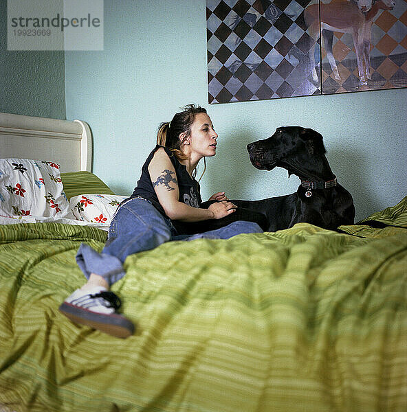 Junge Frau und ihr Hund starren einander an  während sie auf dem Bett liegen.