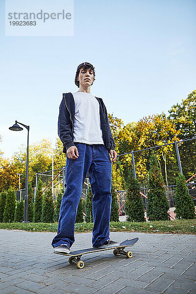 Junger Mann steht auf einem Skateboard im Park