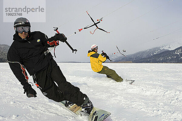 Zwei Männer mittleren Alters beim Snowkiten nebeneinander in Alaska.