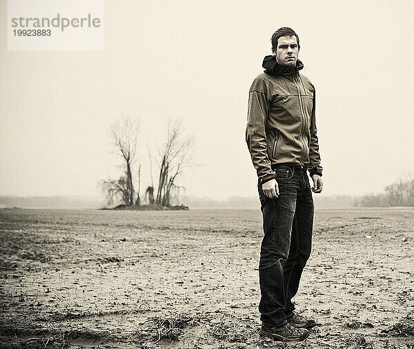 Ein junger Mann steht an einem bewölkten  nassen  trostlosen und trostlosen Tag allein auf einem Feld.