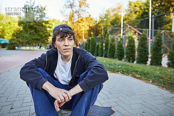 Junger Mann sitzt auf Skateboard im Park