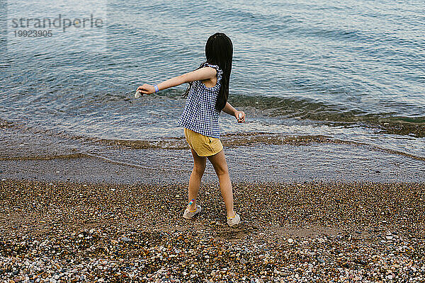 Gemischtrassiges Mädchen wirft Steine ??vom felsigen Strand in den See