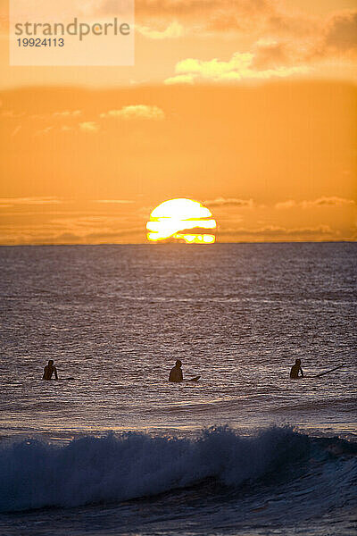 Silhouetten von Surfern in der untergehenden Sonne auf Hawaii.