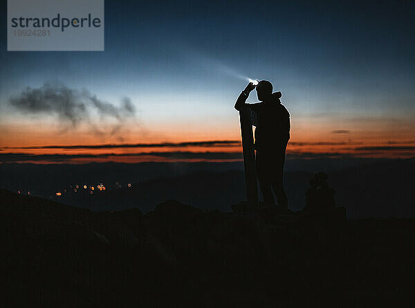 Mann mit Scheinwerferlicht  Silhouette gegen Sonnenuntergang beim Wandern