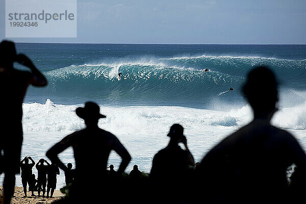 Silhouetten von Zuschauern  die Surfern beim Reiten riesiger Wellen an der weltberühmten Banzai-Pipeline an der Nordküste von Oahu  Hawaii  USA  zuschauen