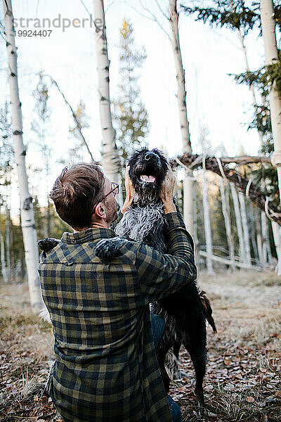 Fröhlicher Moment  als ein Mann seinen schwarzen Hund im Wald umarmt