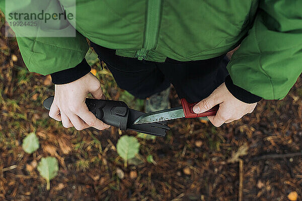 Junge hält ein Messer bereit  um einen Stock im Wald zu schärfen