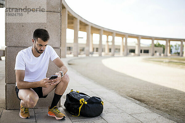 Junger Fitness-Mann-Läufer  der mit einer Sporttasche SMS schreibt.