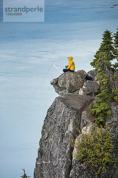 Rucksacktourist sitzt auf einem felsigen Gipfel und genießt den Blick auf den Howe Sound