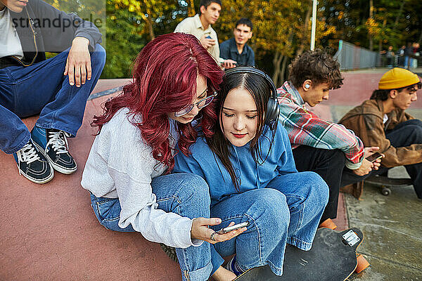 Zwei Mädchen schauen im Skatepark aufs Telefon