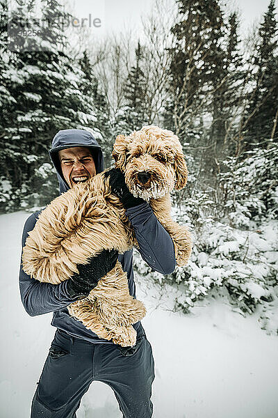 Junger Mann hält seinen Labradoodle-Hund beim Spaziergang im Schnee und in der Kälte