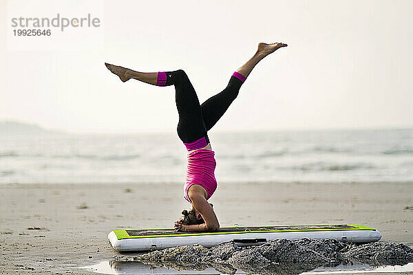 Frau macht Handstand  während sie Yoga am Strand macht