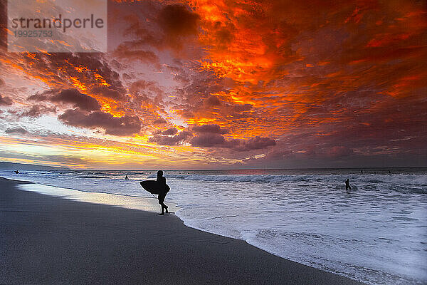 Silhouette eines Surfers mit Surfbrett im Ehukai Beach Park bei Sonnenuntergang  Oahu  Hawaii  USA