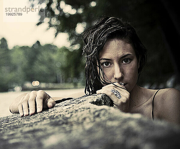 Eine junge Frau mit nassen Haaren liegt neben einem Felsen  ihre Hand bedeckt teilweise ihr Gesicht  an einem See in Maine.