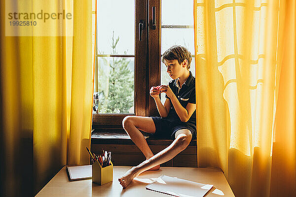 Ruhiger  nachdenklicher Junge  der an einem sonnigen Tag auf einer Fensterbank sitzt