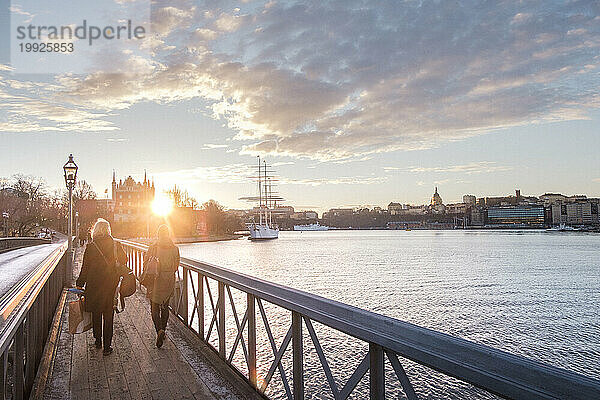 Zwei Frauen gehen bei Sonnenuntergang über die Brücke über den Fluss  Stockholm  Schweden