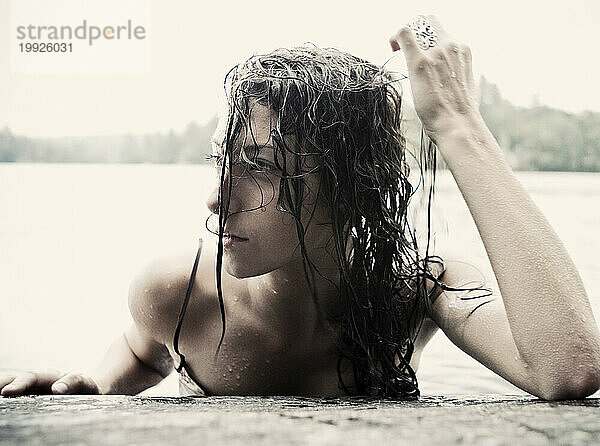 Eine junge Frau mit nassen Haaren taucht nach dem Schwimmen aus einem See