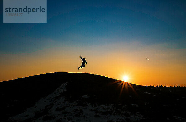 Silhouette eines kleinen Kindes  das bei Sonnenuntergang von einem Hügel springt