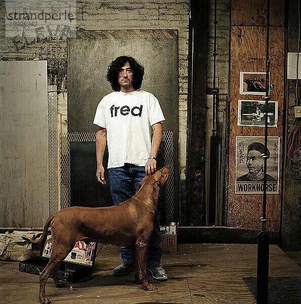 Ein Mann steht mit seinem Hund in seiner Werkstatt.