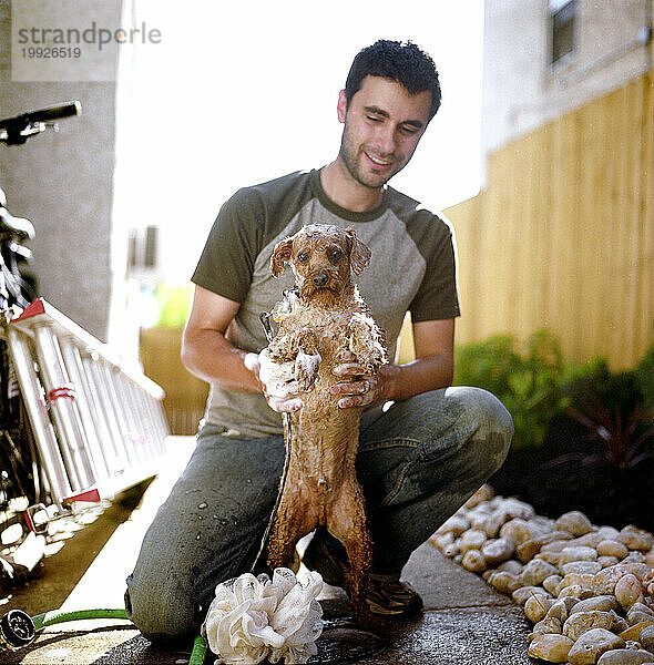 A young man gives his dog  a toy poodle  a bath in his backyard in Philadelphia  Pennsylvania
