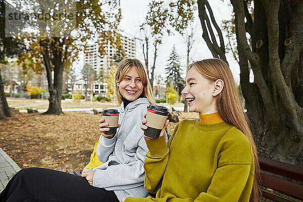 Zwei lachende junge Frauen mit Getränken im Park im Herbst