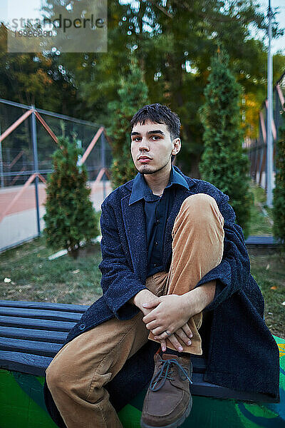 Junger Mann in dunklem Mantel sitzt auf einer Bank
