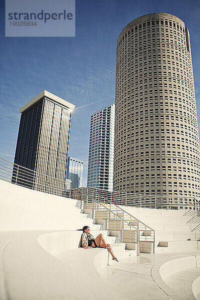 Eine Frau entspannt in der Sonne in einem Amphitheater  während die Wolkenkratzer der Skyline von Tampa  Florida  sie überragen.