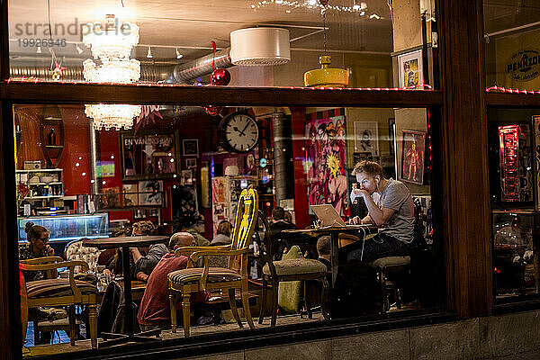 Fensteransicht der Bar bei Nacht mit Mann  der drinnen einen Laptop benutzt  Stockholm  Schweden