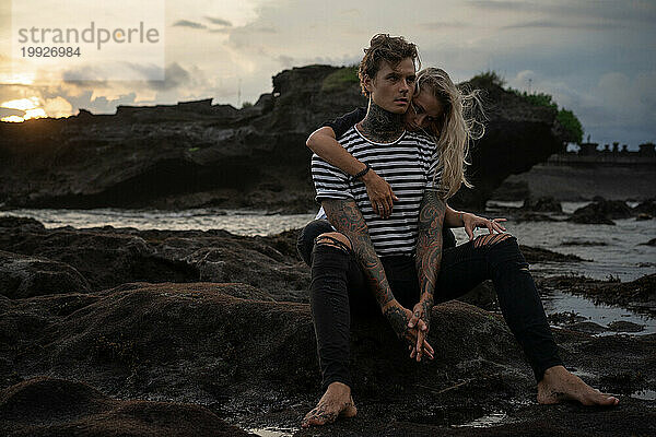Verliebtes Paar am Strand und beobachtet den Sonnenuntergang  Bali. Tätowierter Mann.
