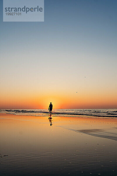 Silhouette eines Mannes  der bei Sonnenaufgang am Hilton Head Island Beach spaziert