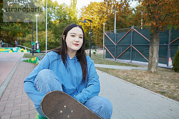 Mädchen sitzt mit Skateboard auf Bank im Skatepark