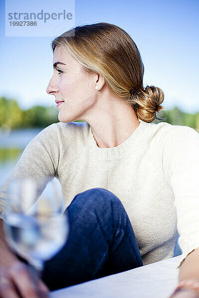Eine Frau genießt ihr Abendessen an einem Tisch im Freien mit einem malerischen See im Hintergrund.