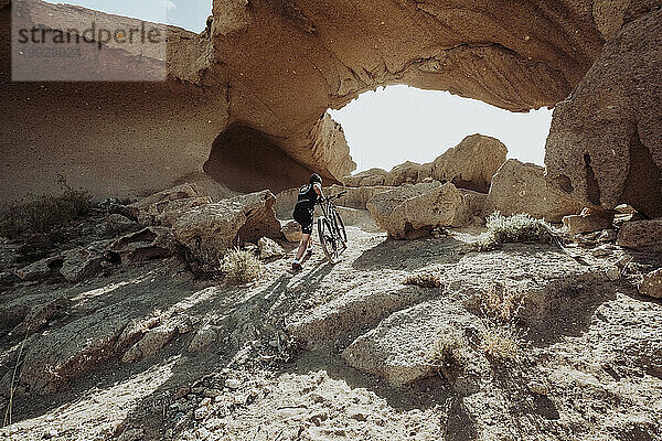 Mann wandert mit seinem Mountainbike in der Wüste in Richtung Felsbogen  Teneriffa  Kanarische Inseln  Spanien