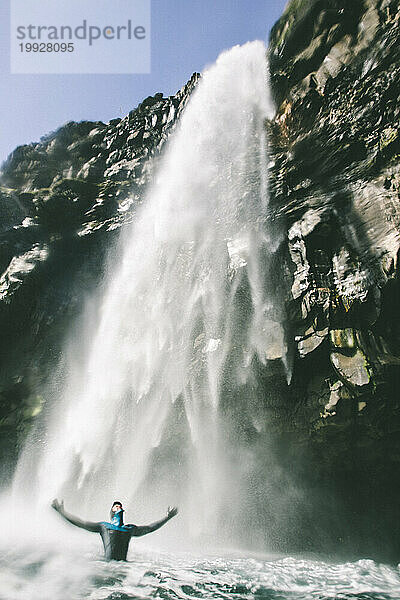 Ein Mann im Neoprenanzug steht unter einem großen Wasserfall auf den Färöer-Inseln