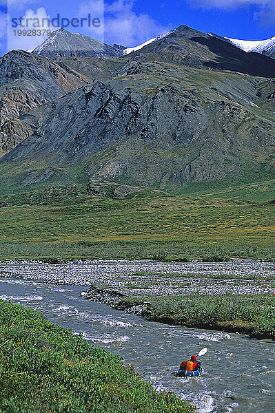 Ein Kajakfahrer paddelt mit seinem Packfloß einen Fluss hinunter vor den Bergen  Arctic National Wildlife Refuge  Alaska.