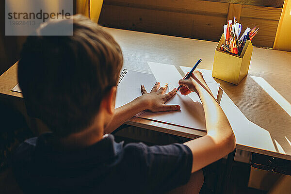Draufsicht auf einen Jungen  der seine Hand mit einem Bleistift auf einem Papier umkreist