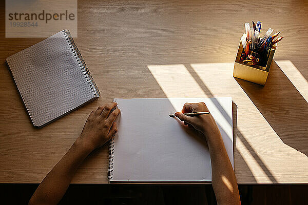 Draufsicht auf einen Jungen  der anfängt  auf einem weißen Papier zu zeichnen