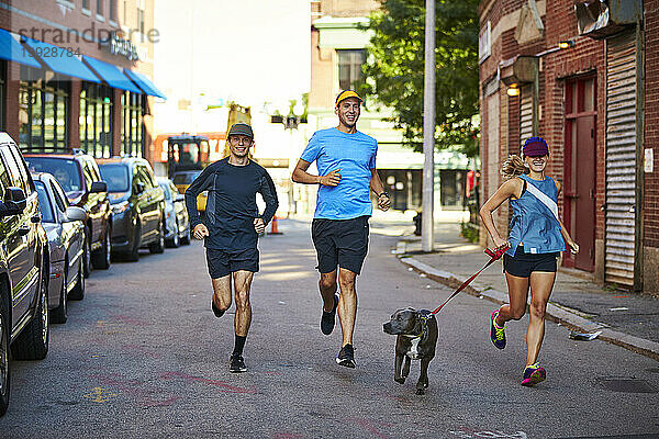 Eine Gruppe von drei Läufern läuft mit einem Hund