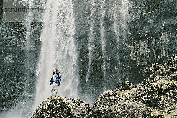 Ein Mann steht auf einem Felsen neben einem Wasserfall auf den Färöer-Inseln