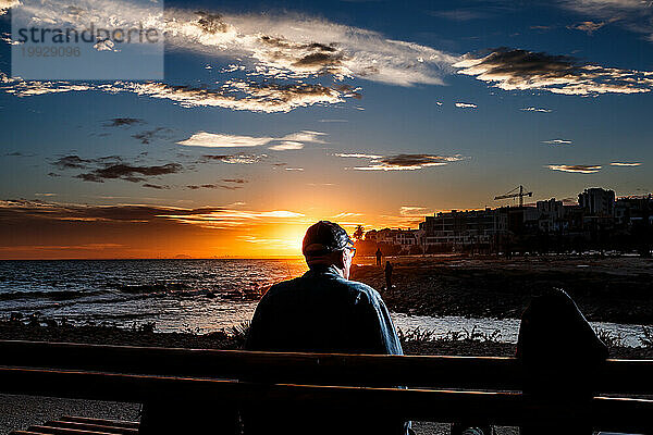 Ruhiger Mann  der auf einer Bank sitzt und den Sonnenuntergang beobachtet