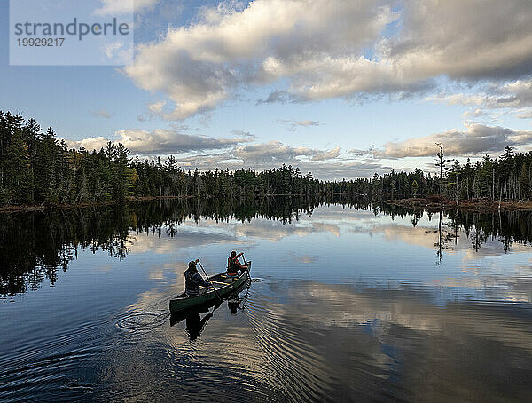Paar schwimmt im Kanu auf einem ruhigen See in den Wäldern von Maine.