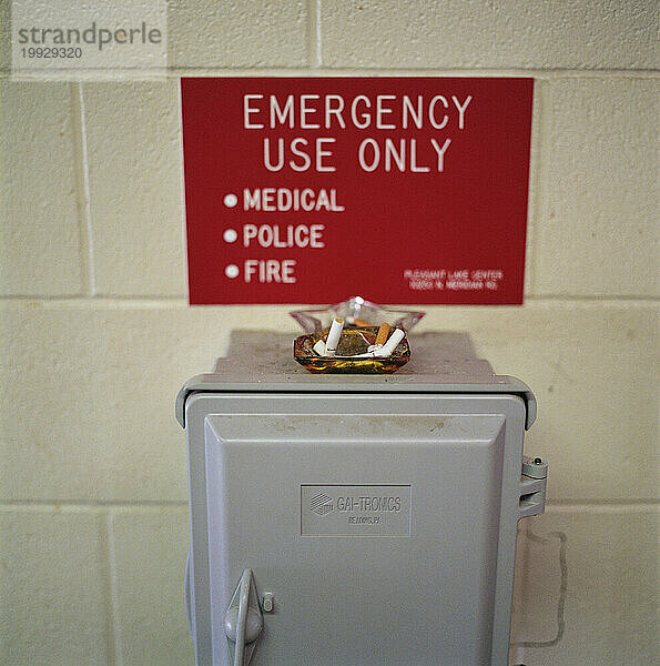 Ein voller Aschenbecher steht vor einem Schild mit der Aufschrift „