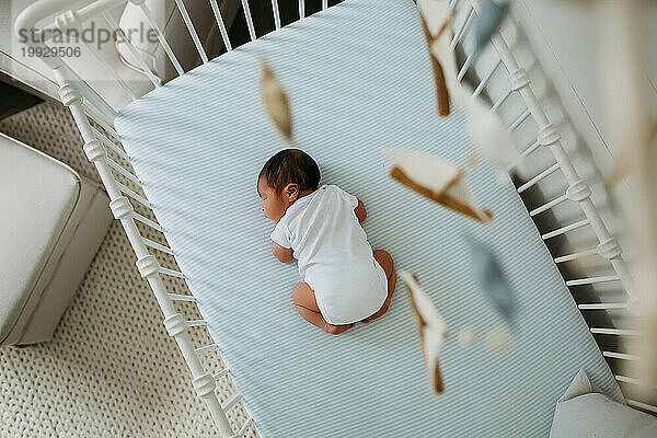 Blick von oben auf ein neugeborenes Baby in seinem Kinderbett mit einem Mobile im Blick