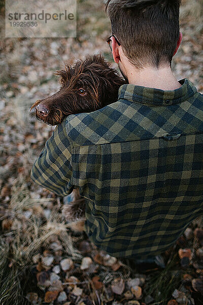 Man holding a Griffon dog over shoulder in the forest
