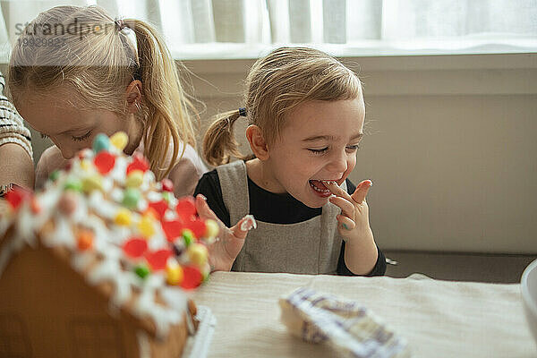 Mädchen kichert beim Dekorieren eines Lebkuchenhauses mit der Familie