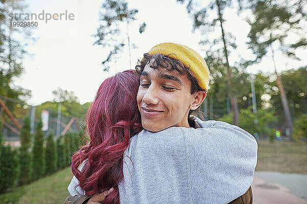 Junger Mann umarmt Mädchen mit roten Haaren im Park